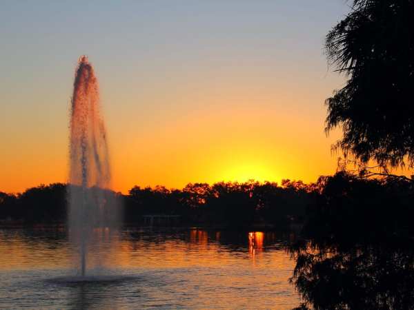 a fountain in front of a sunset over a body of water