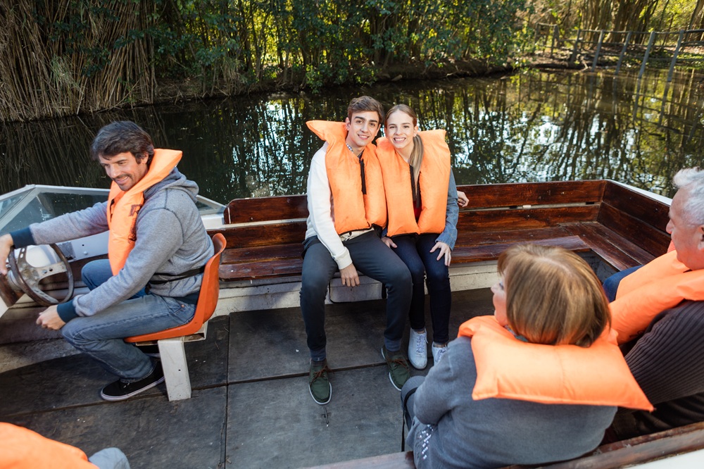 Group on a boat wearing orange life jackets, with trees visible in the background.